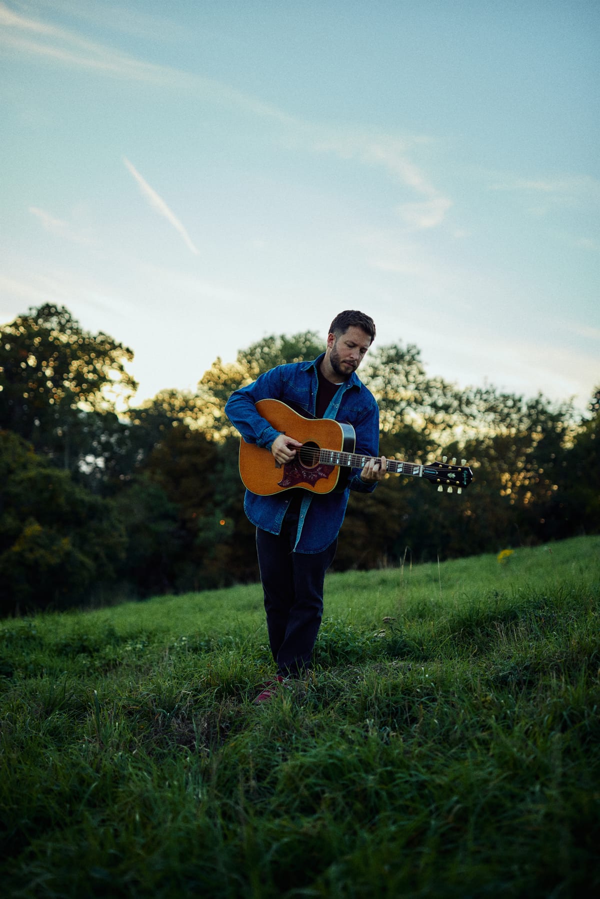 Josh Smith playing acoustic guitar on a hillside under an open sky
