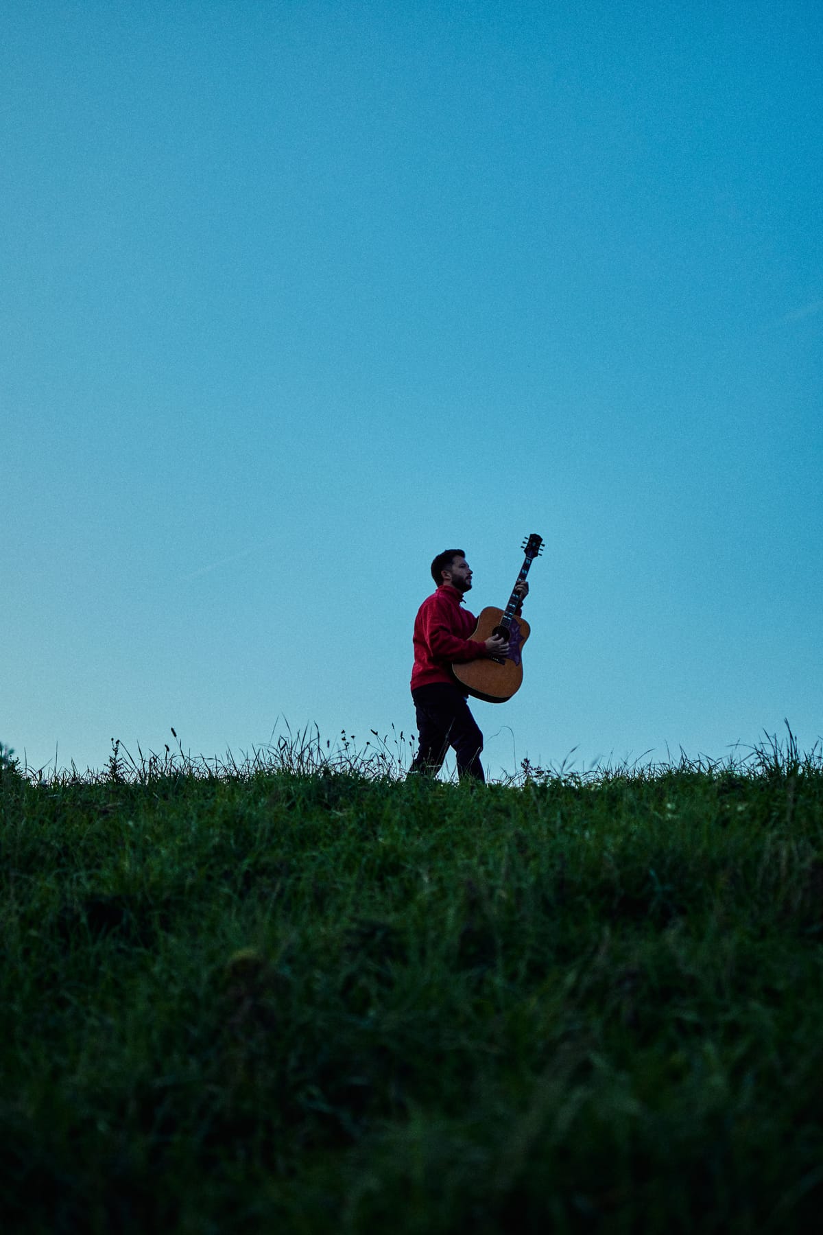 Josh Smith walking across a hilltop carrying his guitar
