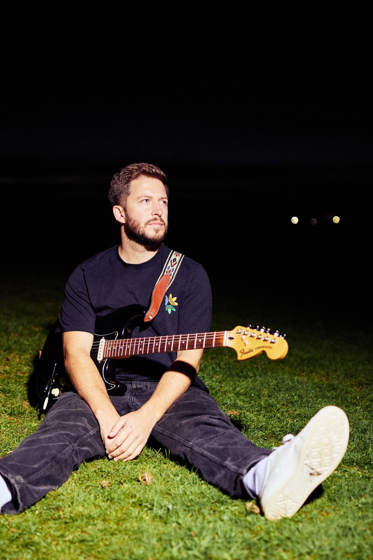 Josh Smith sitting on the grass at night with an electric guitar